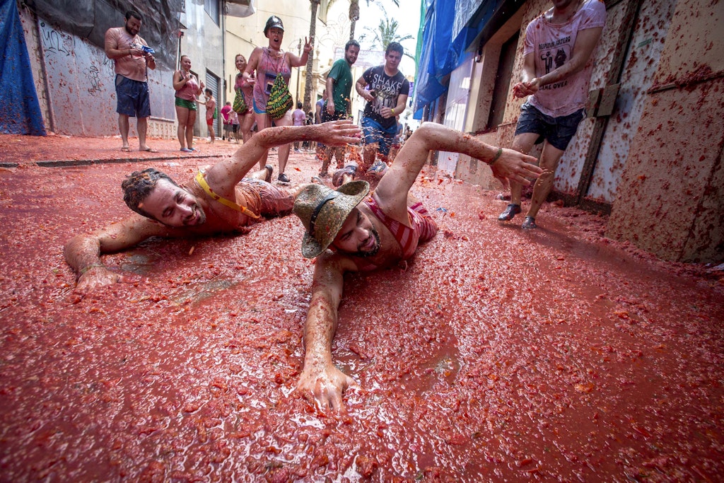 Revellers mock a swim in tomato pulp during the annual "tomatina" festivities in the village of Bunol, near Valencia on August 26, 2015. Some 22,000 revellers hurled 150 tonnes of squashed tomatoes at each other drenching the streets in red in a gigantic Spanish food fight marking the 70th annual "Tomatina" battle.    AFP PHOTO / BIEL ALINO / AFP / BIEL ALINO        (Photo credit should read BIEL ALINO/AFP via Getty Images)