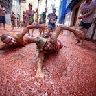 Revellers mock a swim in tomato pulp during the annual "tomatina" festivities in the village of Bunol, near Valencia on August 26, 2015. Some 22,000 revellers hurled 150 tonnes of squashed tomatoes at each other drenching the streets in red in a gigantic Spanish food fight marking the 70th annual "Tomatina" battle.    AFP PHOTO / BIEL ALINO / AFP / BIEL ALINO        (Photo credit should read BIEL ALINO/AFP via Getty Images)