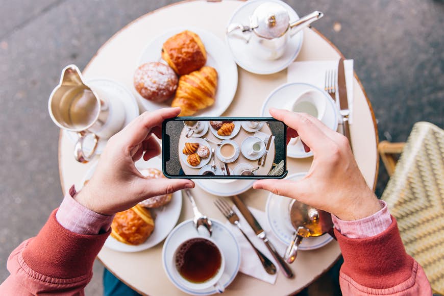 Young man photographing croissant and french breakfast on table in sidewalk cafe in Paris, France