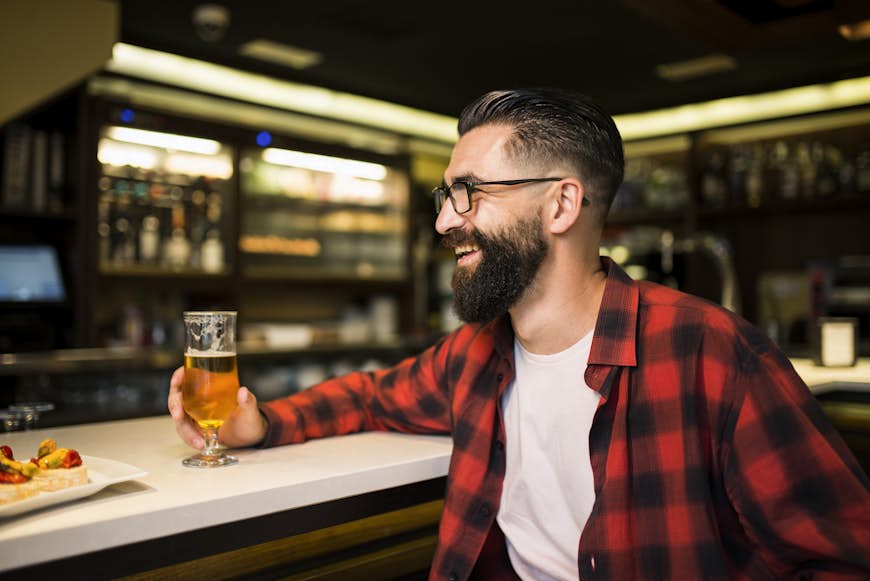 Hipster med ett glas öl och tapas som sitter vid disken på en pub