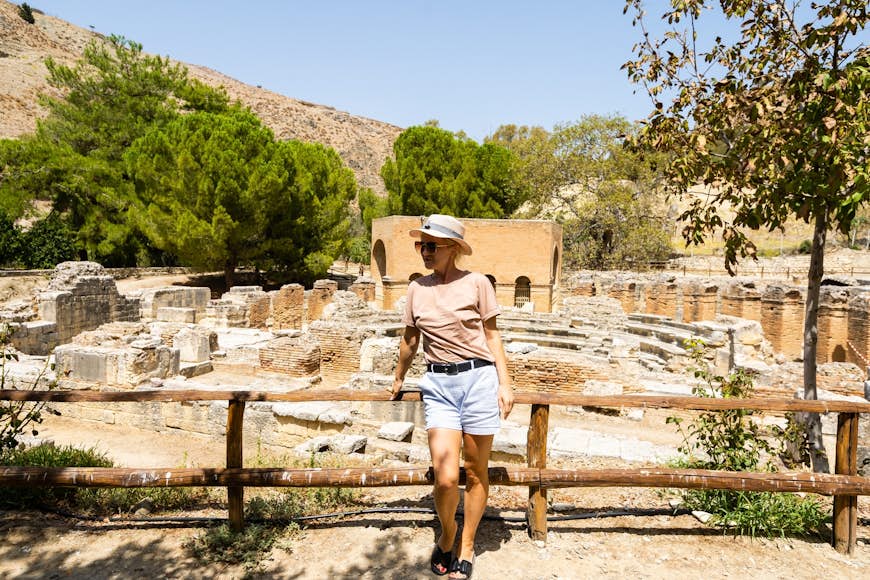 Une femme se tient dos à une série de ruines romaines en Crète