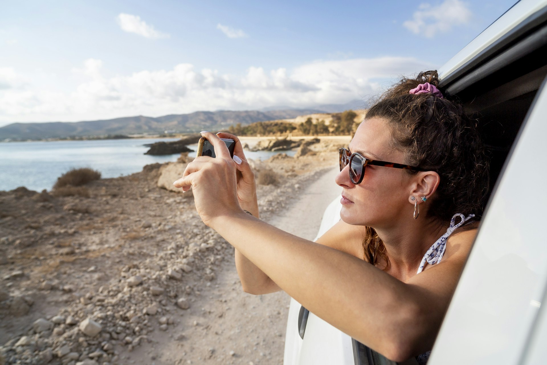 A woman taking a photo through a car window near Balos Beach, Crete