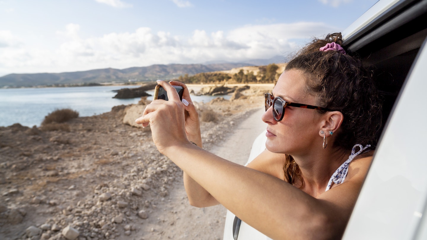 young woman riding in a car and taking photo with smartphone