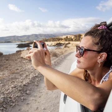 young woman riding in a car and taking photo with smartphone