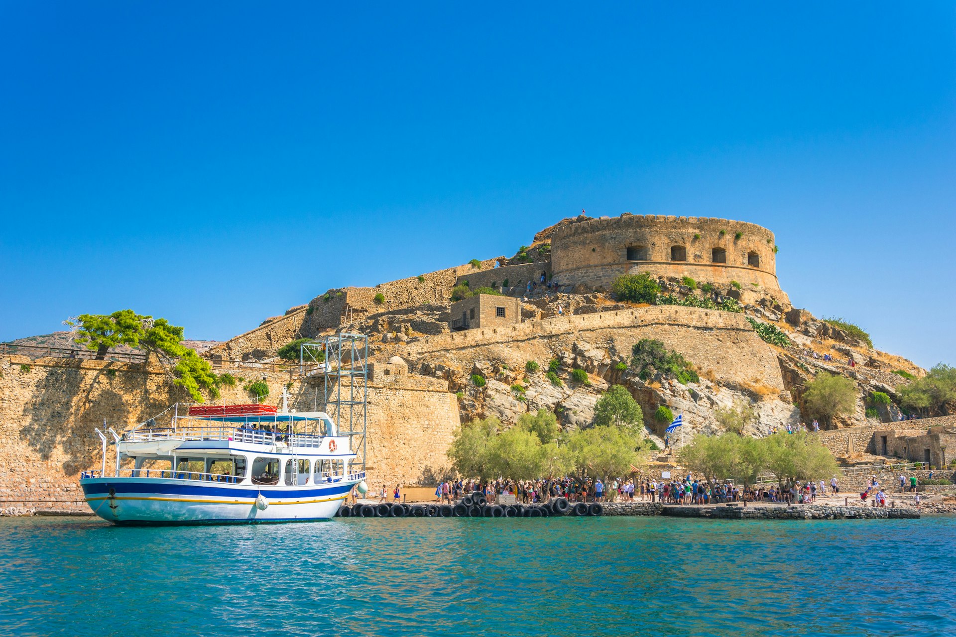 View of the island of Spinalonga with a calm sea and passengers disembarking from a ferry