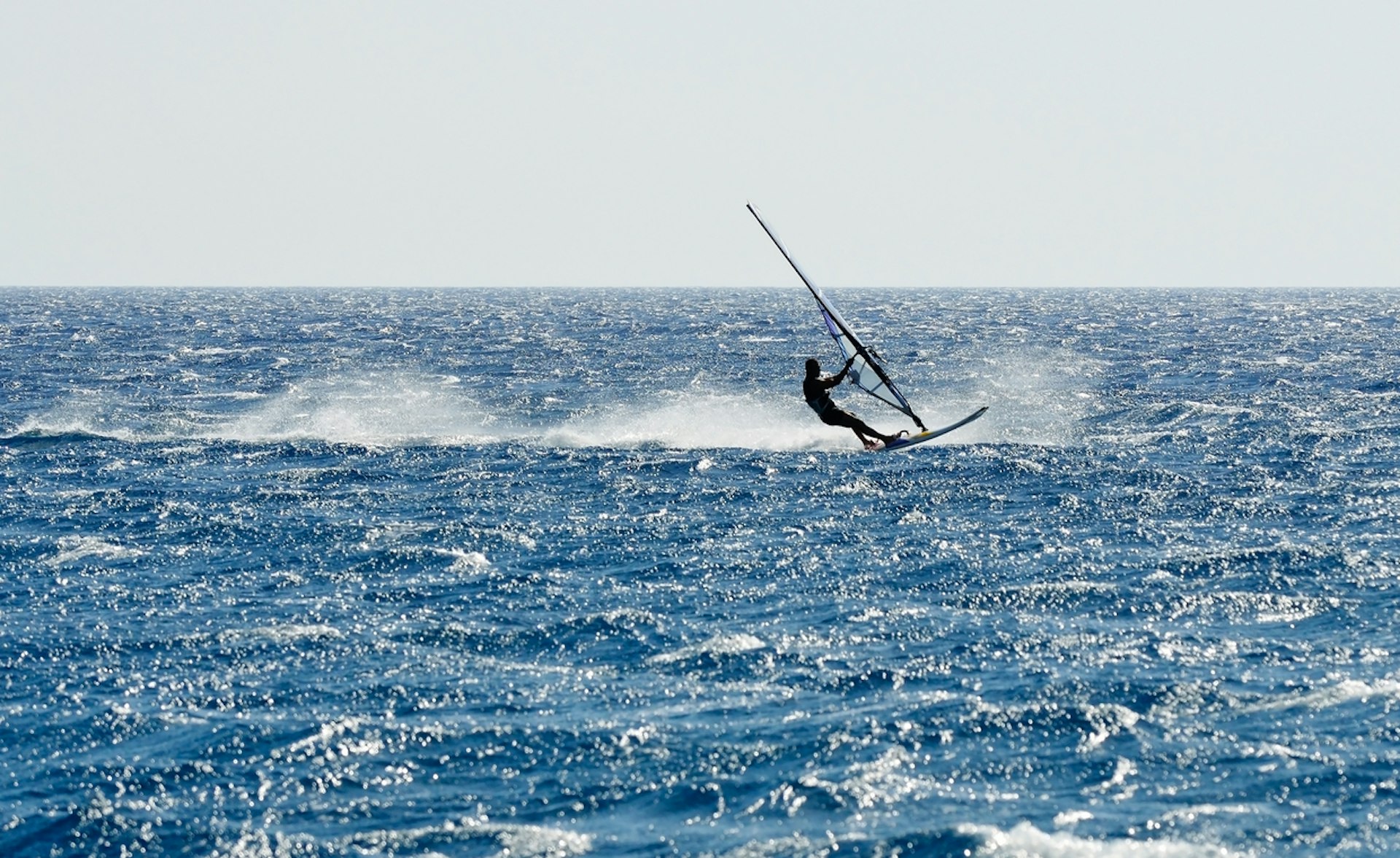 A windsurfer speeds over choppy waters