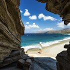 Beautiful woman with sunhat contemplating the sea out of a cave on Triopetra beach, Plakias, Crete, Greece