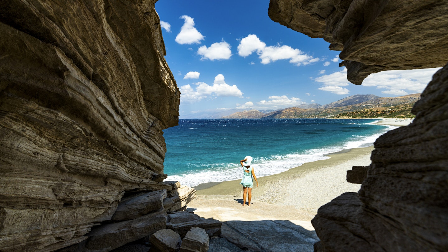 Beautiful woman with sunhat contemplating the sea out of a cave on Triopetra beach, Plakias, Crete, Greece