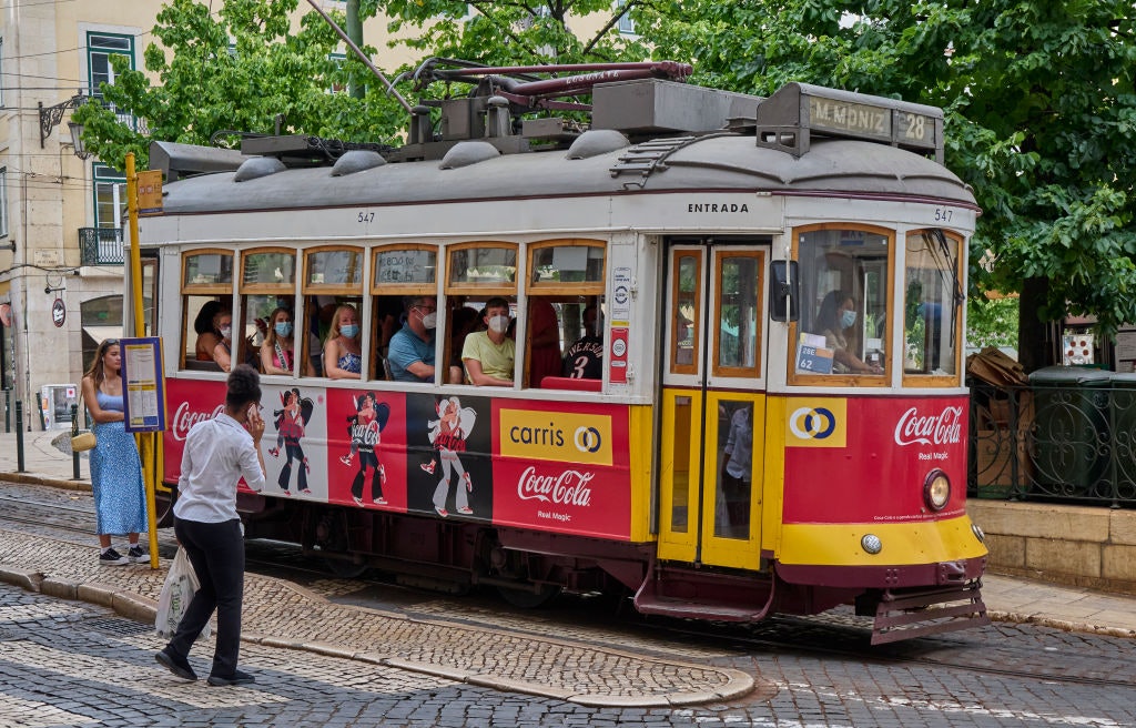 Mask-clad tourists ride by Praça Camoes on a Line 28 tram