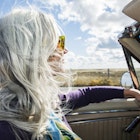 Woman from the baby boomer generation driving in an antique convertible car on a sunny fall day with her long, silver gray hair blowing in the wind.