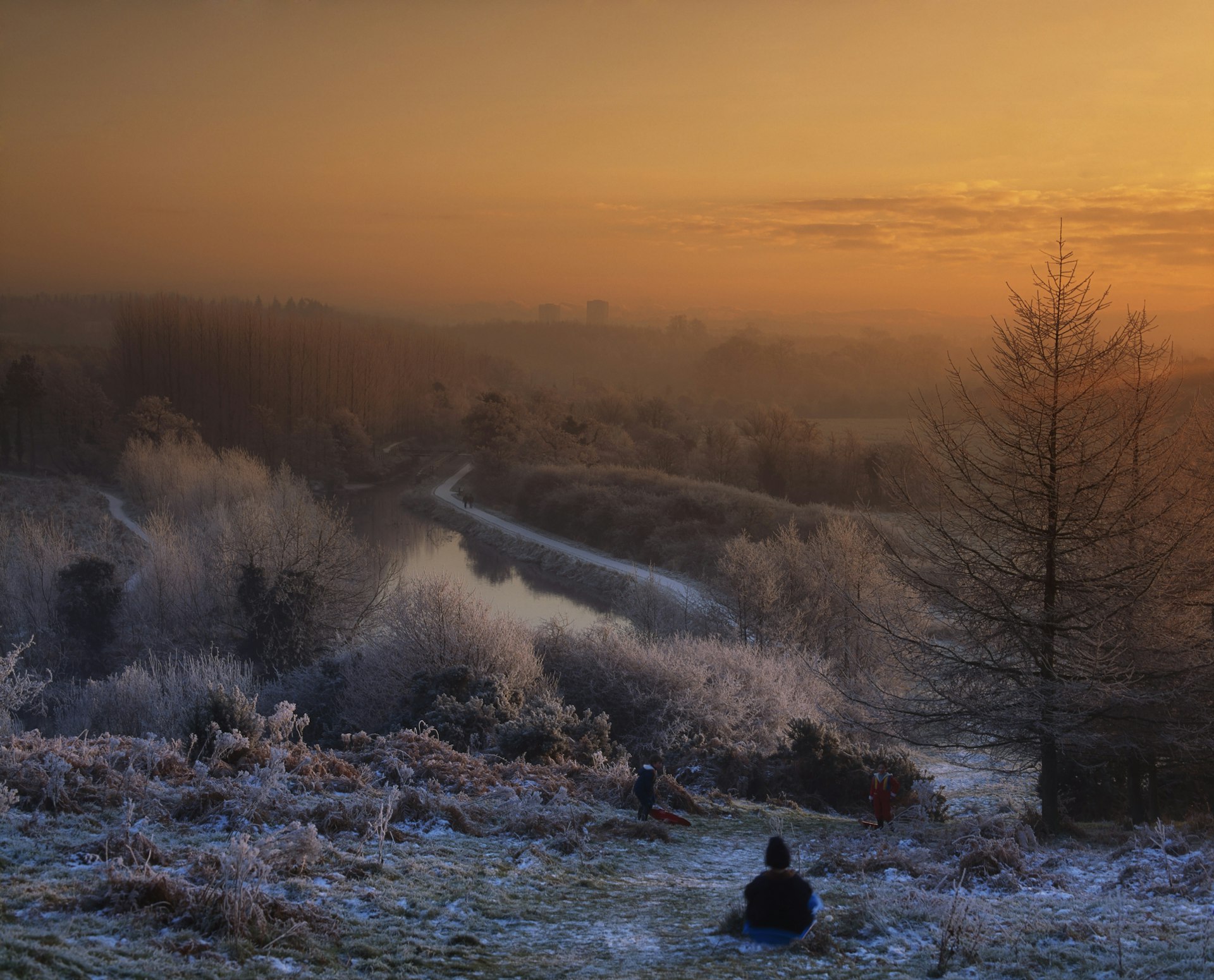 An orange sun sets across the frost-covered hills and trees of Lagan Meadows in Belfast 