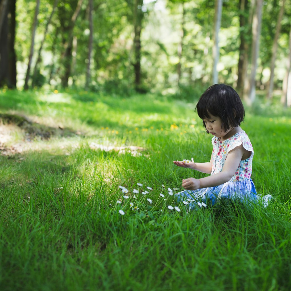 Little girl sits on the grass of a forest in Belfast, Northern Ireland.