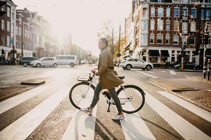Millennial Japanese commuter in the city with bicycle, crossing the street in Amsterdam