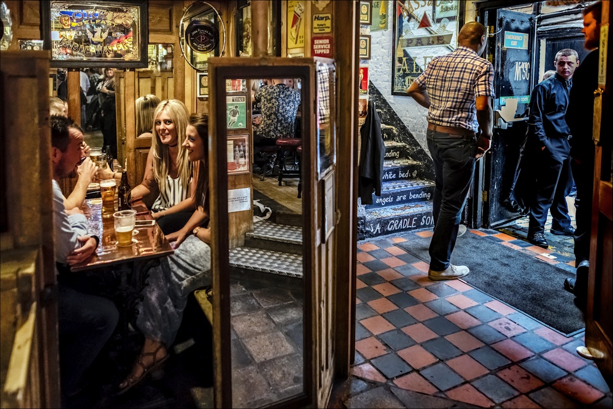 Patrons sit in a snug at the Duke of York, a classic pub down a cobbled alley with mirrored bar and advertising signs.