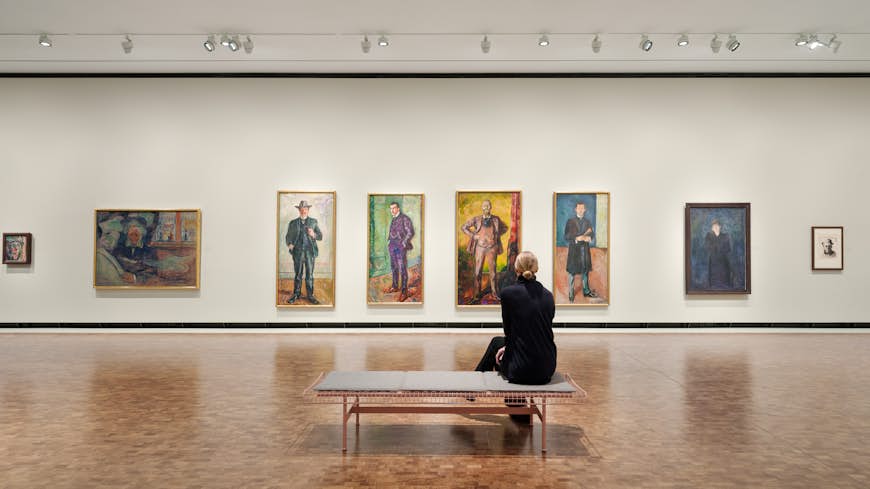 A woman sits and takes a series of four paintings on the back wall of the new Munch Museum in Oslo.