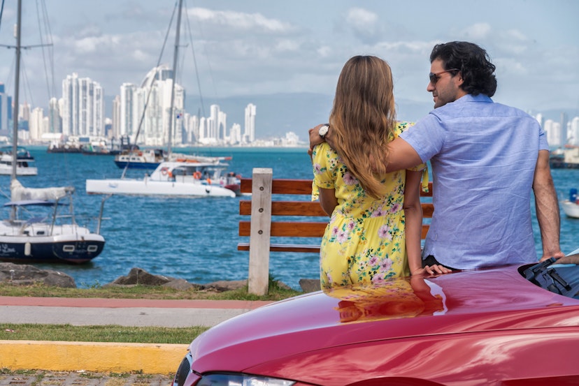 Latin Couple leaning on the side of a red car watching Panama city