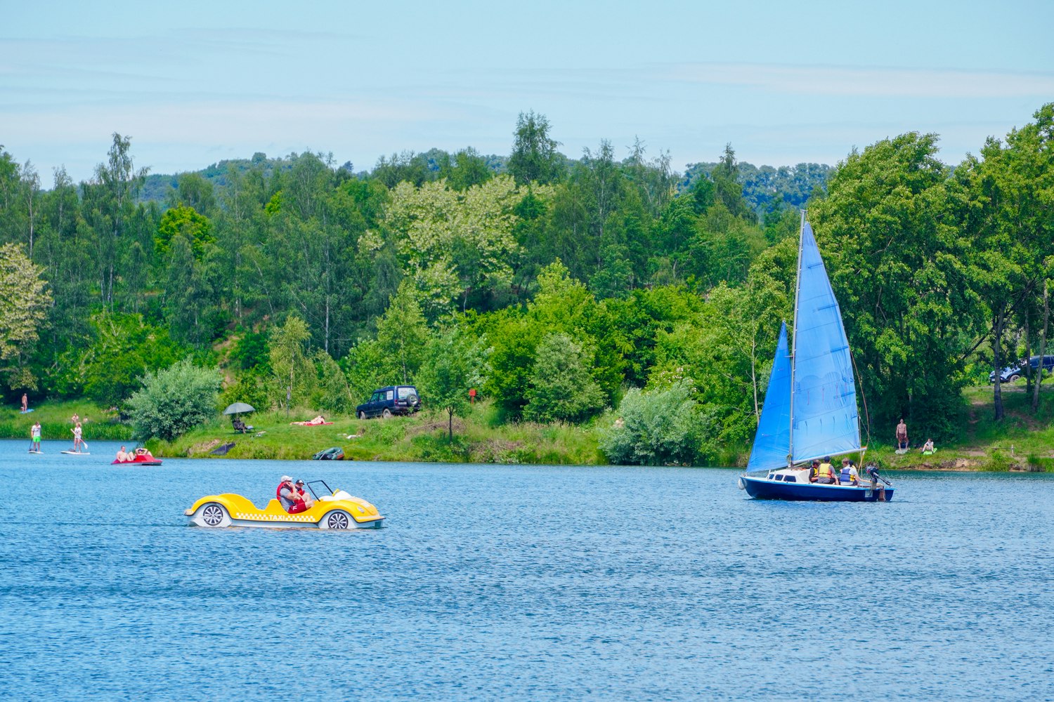 A small sail boat and a peddle boat on a lake on a summer's day