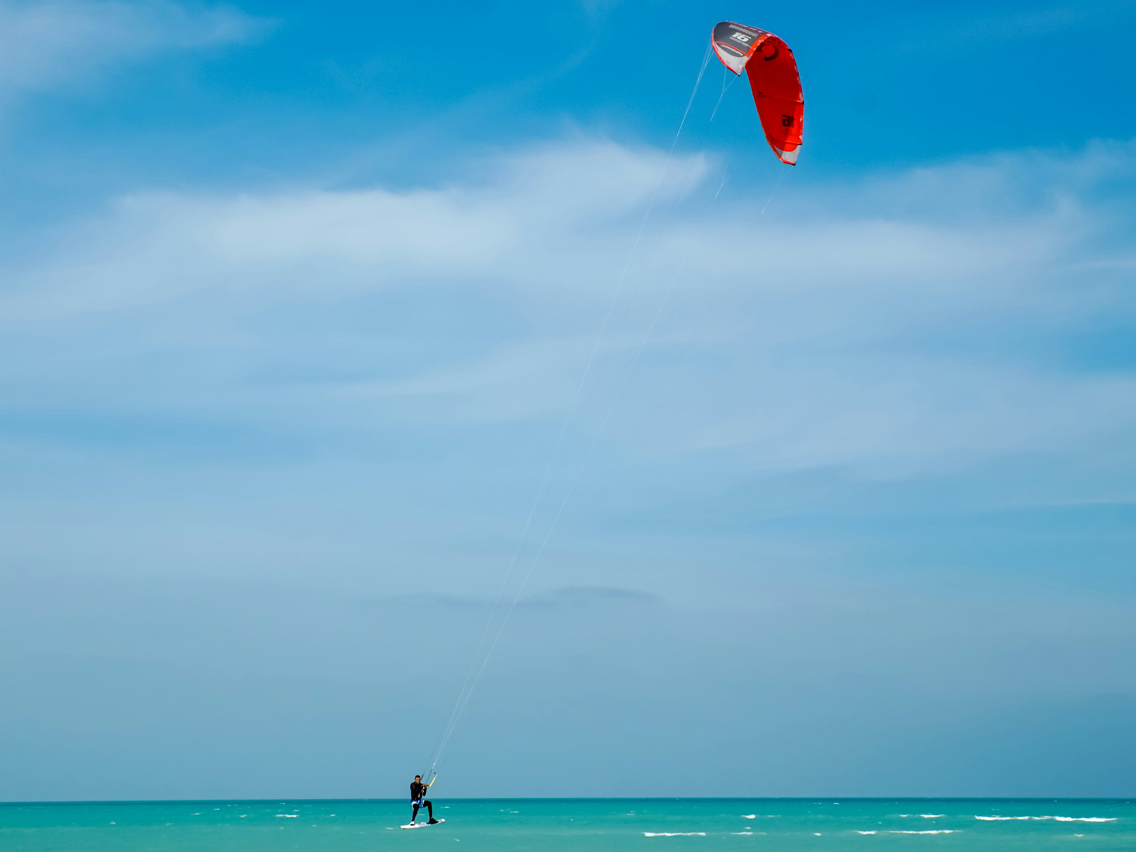 A kitesurfer under a red sail is carried along by the wind on the turquoise waters of Fuwairit Beach, Qatar 