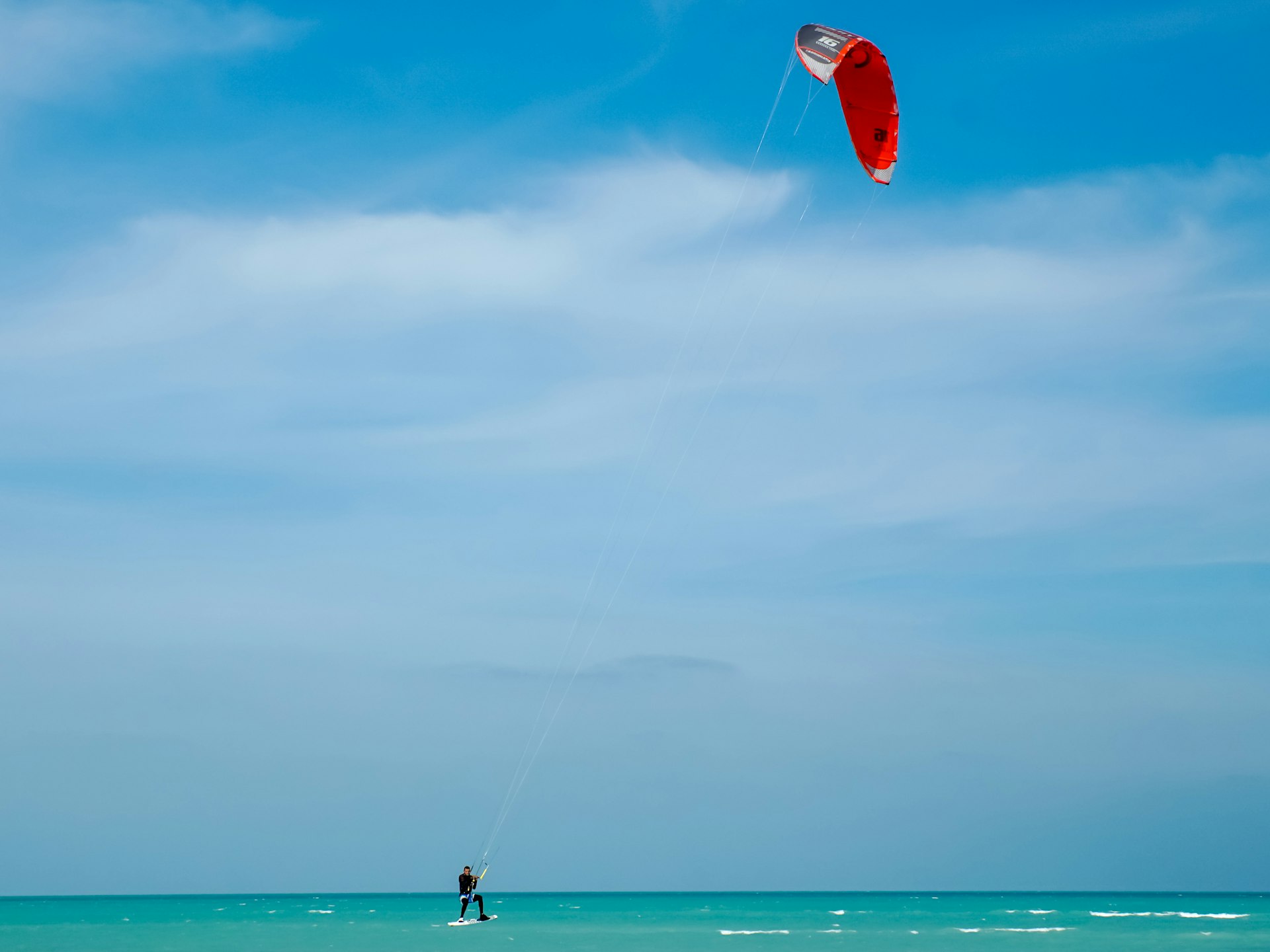 A kitesurfer under a red sail is carried along by the wind on the turquoise waters of Fuwairit Beach, Qatar 