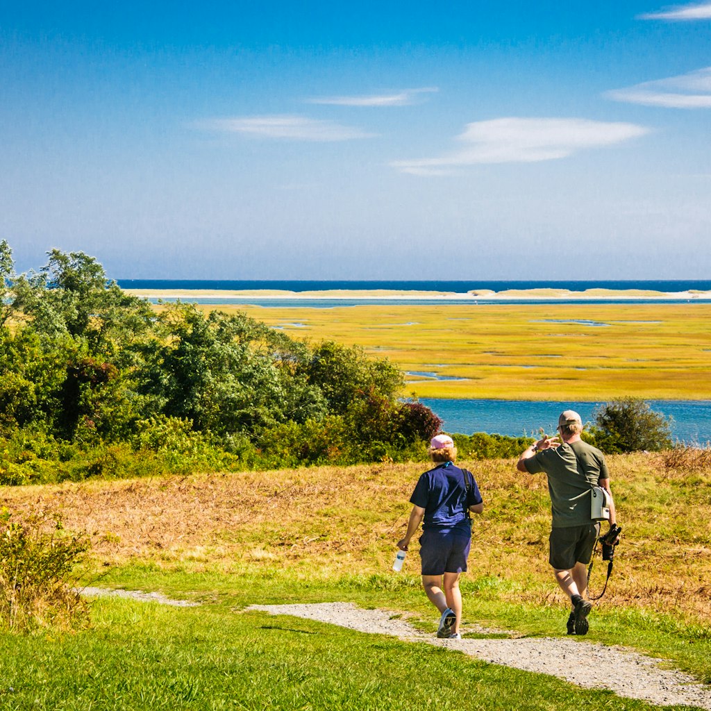 Eastham, Massachusetts, USA -September 26, 2019- A middle aged couple armed with cameras, tripods, binoculars and water bottles set out on a hike through the low lying salt marshes of the Fort Hill area of the Cape Cod National Seashore on a bright autumn morning.