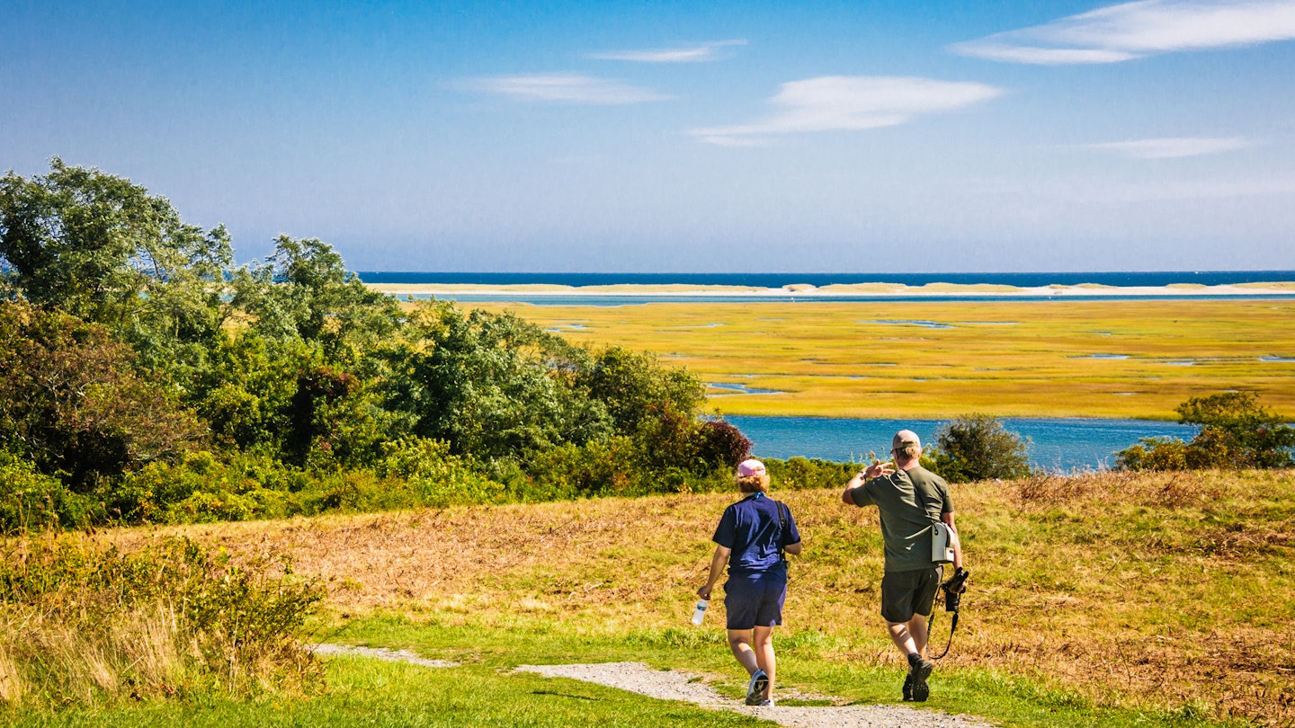 Eastham, Massachusetts, USA -September 26, 2019- A middle aged couple armed with cameras, tripods, binoculars and water bottles set out on a hike through the low lying salt marshes of the Fort Hill area of the Cape Cod National Seashore on a bright autumn morning.