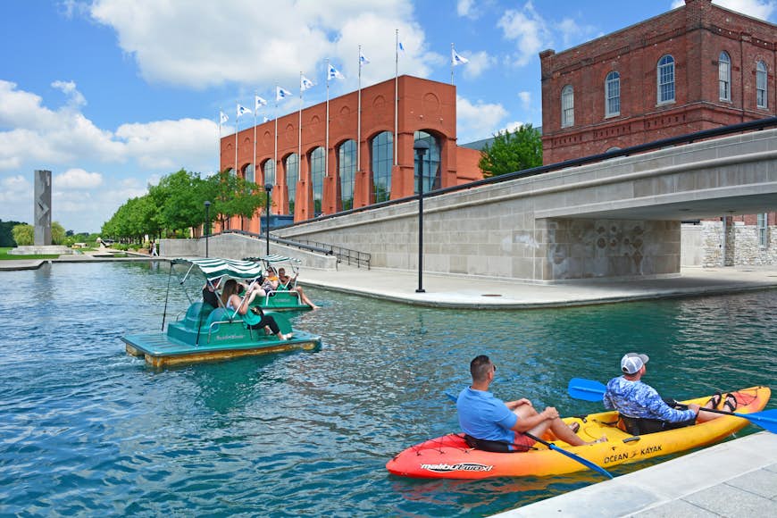 People in paddle boats pass by in a canal in downtown Indianapolis, Indiana, Midwest, USA