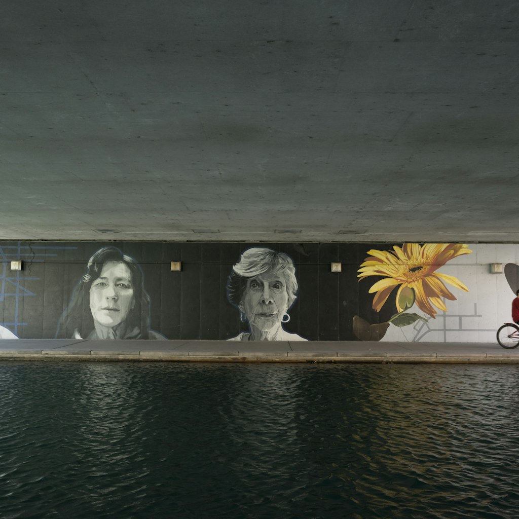 Indianapolis, Indiana, USA - April 10, 2015: Two people ride a tandem bicycle past a mural on the popular Canal Walk in Indianapolis, Indiana. The waterway is part of the historic Indiana Central Canal, constructed in the early 1800s.