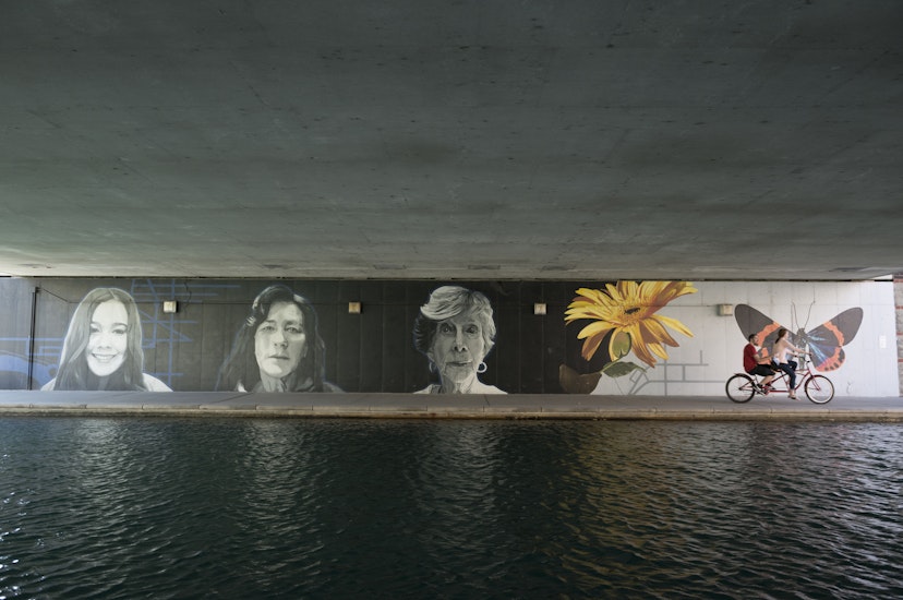 Indianapolis, Indiana, USA - April 10, 2015: Two people ride a tandem bicycle past a mural on the popular Canal Walk in Indianapolis, Indiana. The waterway is part of the historic Indiana Central Canal, constructed in the early 1800s.