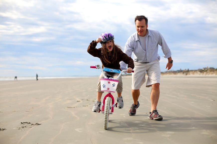 A father and daughter riding a bike on the sand at Kiawah Island, South Carolina 