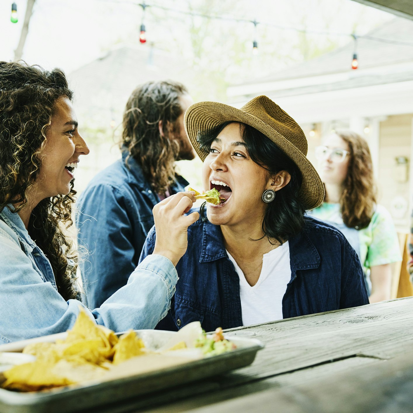 A laughing woman feeds her partner a tortilla chip heaped with guacamole at a food truck