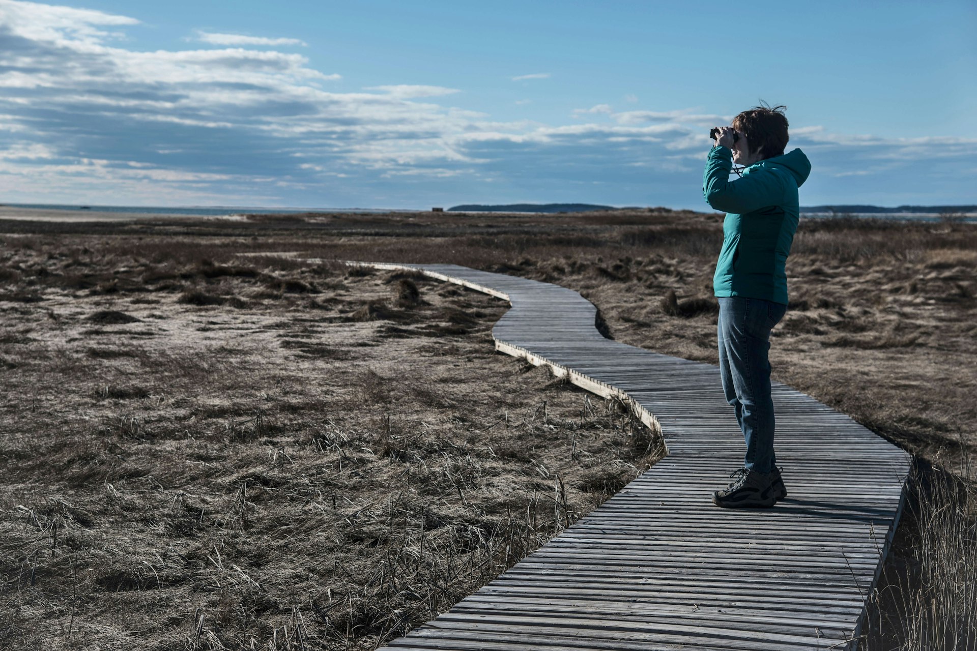 Woman standing on a boardwalk looking through binoculars 