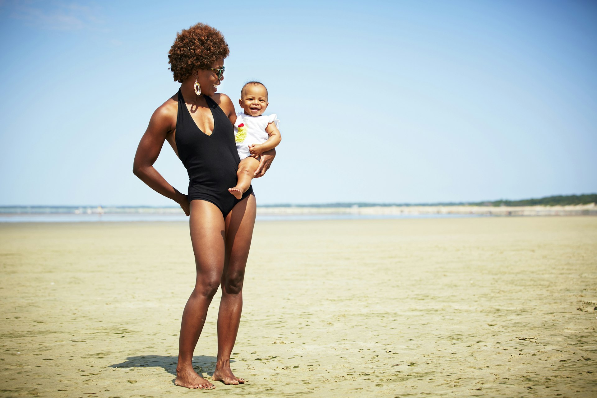 Smiling black mother holding baby girl on an empty beach in Massachusetts where the tide is out