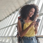 Young woman with backpack checking her boarding schedule at an airport.