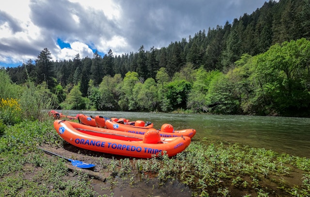 Five inflatable orange boats on the banks of the Rogue River in Oregon