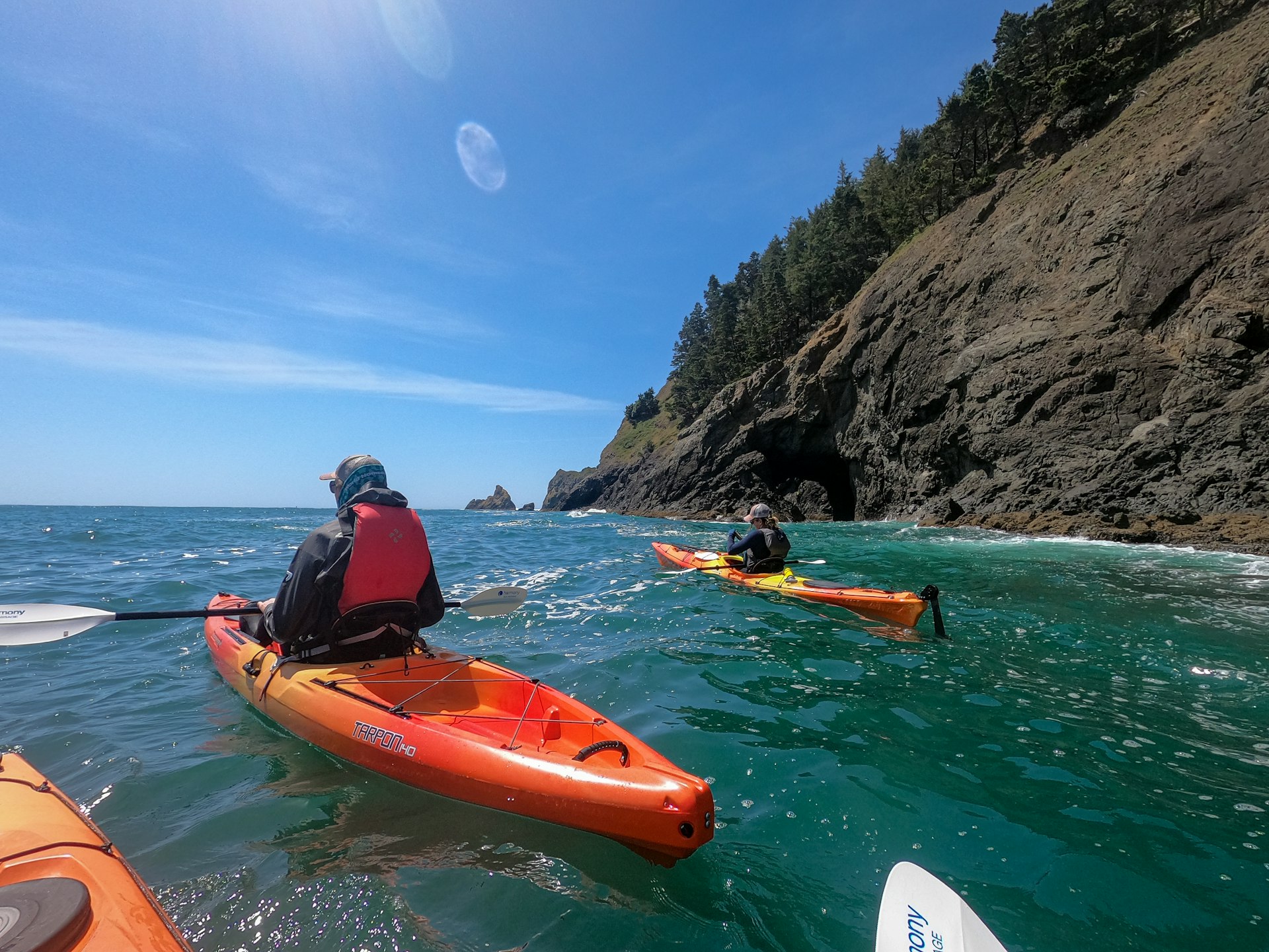 Two people look out to sea while floating in orange kayaks off the Oregon Coast