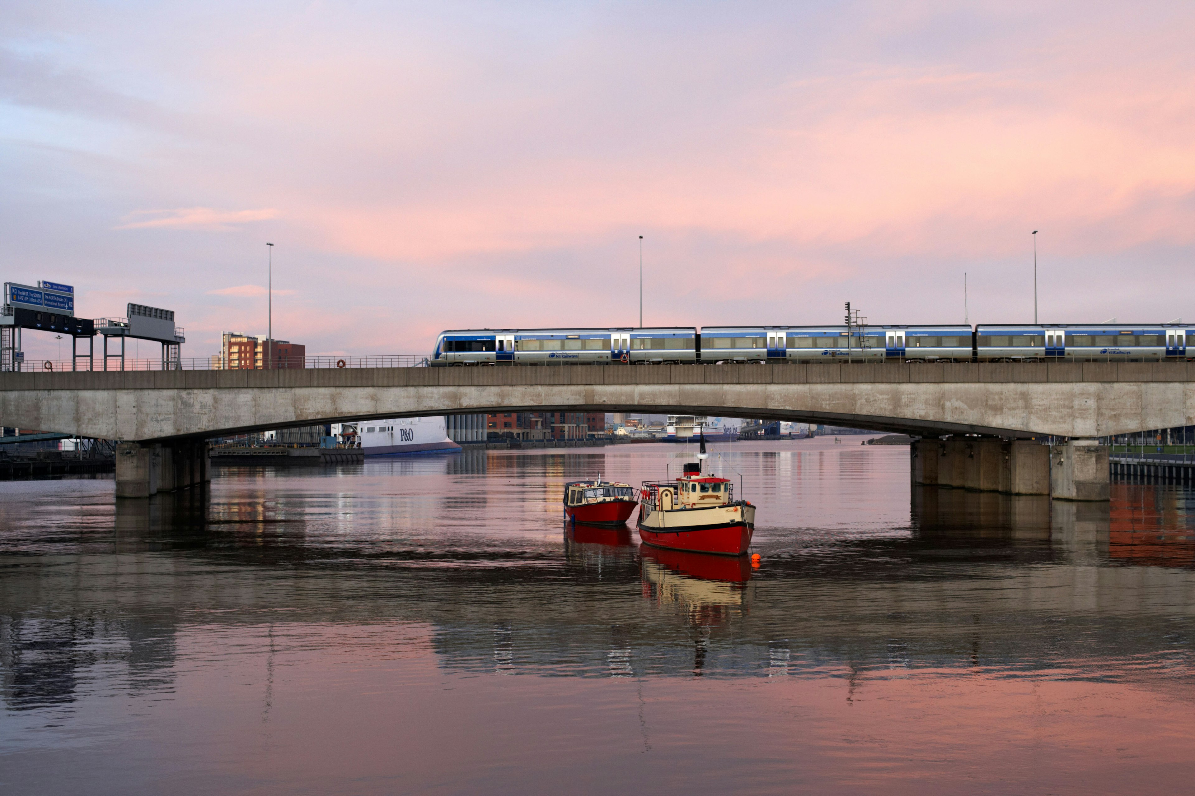 A train on a bridge crossing a river as a small boat sails by