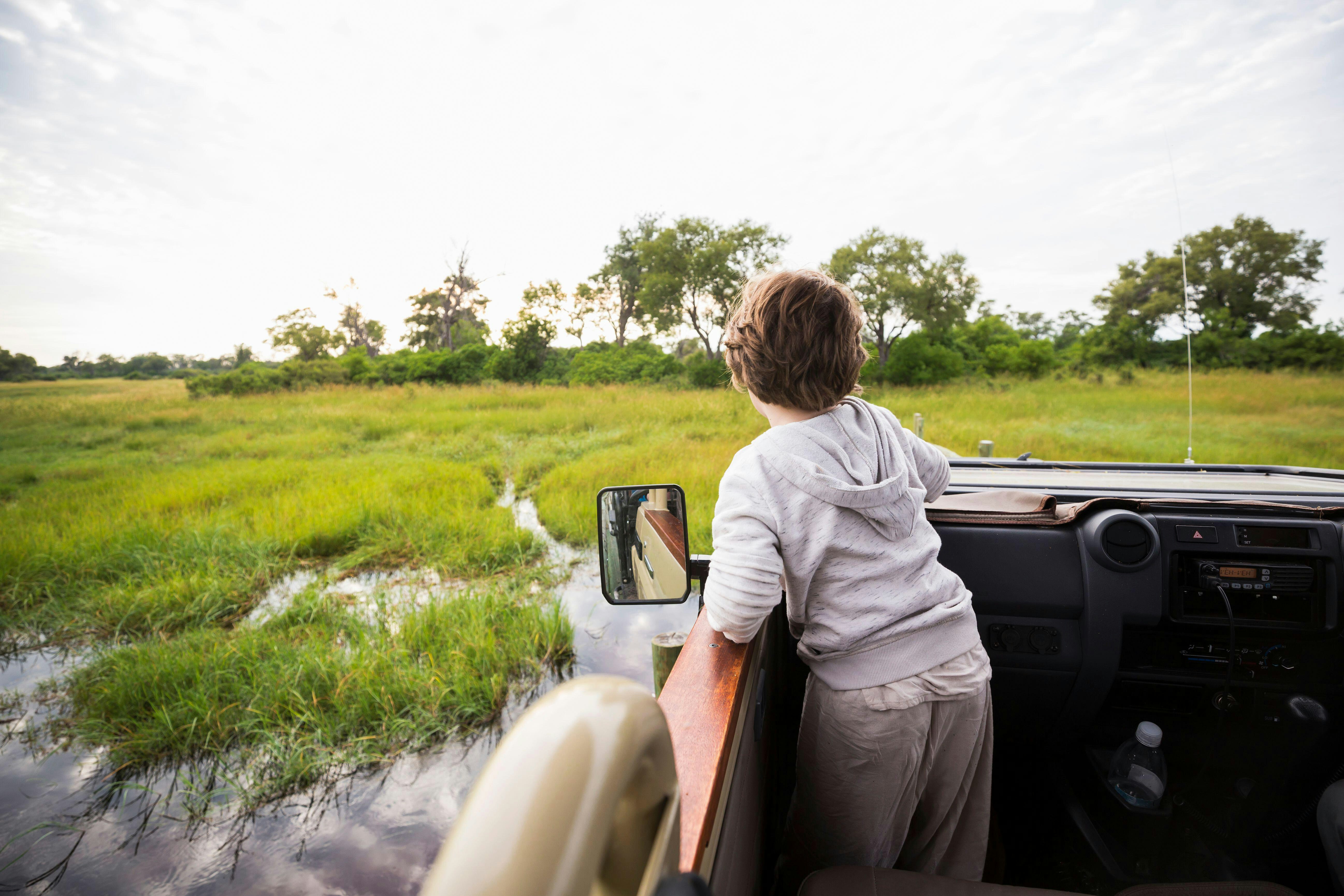 A six year old boy in a safari jeep driving through water in marshes looking for wildlife in Botswana