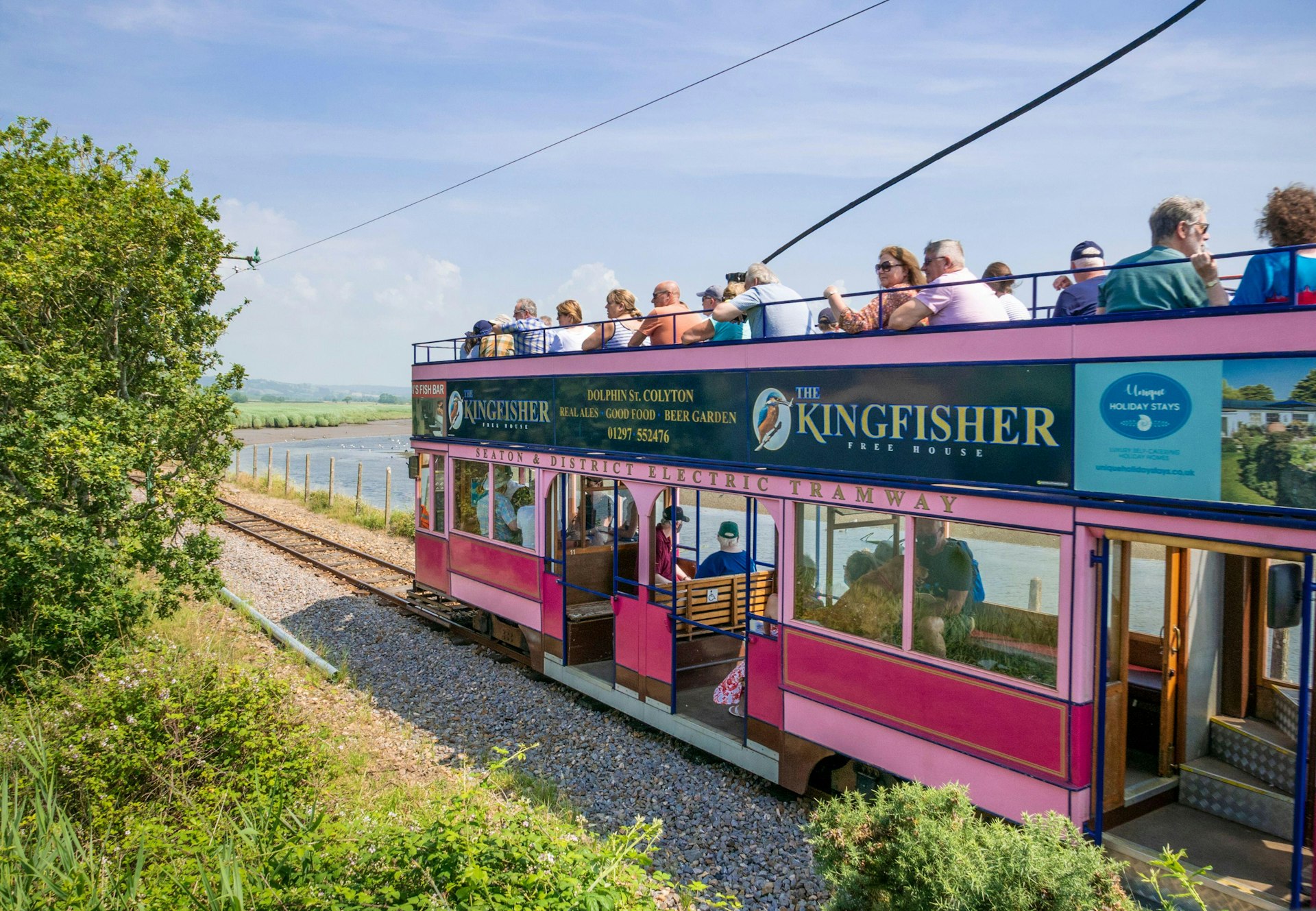 Passengers ride a historic tram on the track beside the Seaton wetlands, Seaton, Devon, England, United Kingdom
