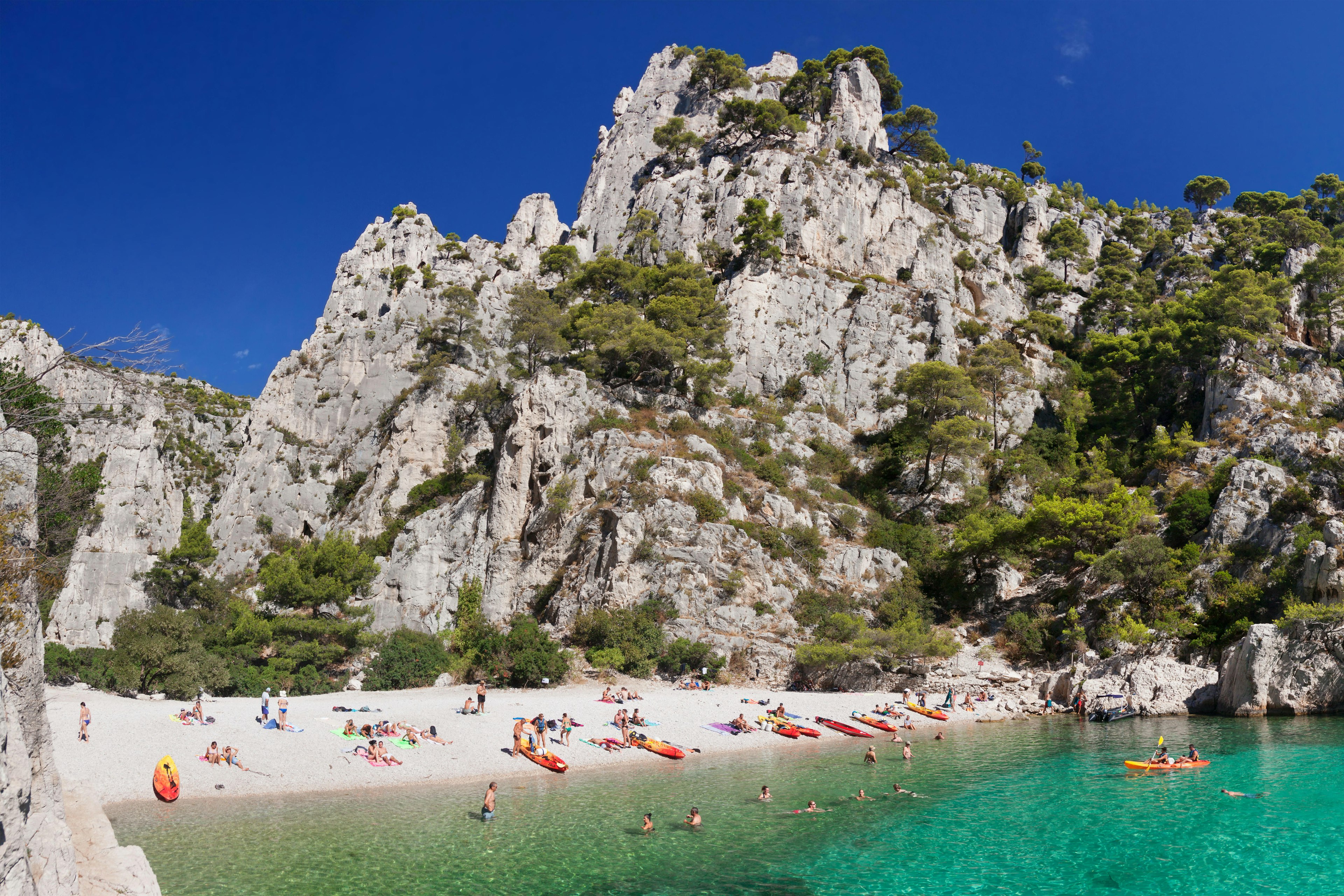 Landscape of a beach with people laying out in the sand and swimming in the sea with rocky cliffs in the background