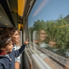 Portrait of a happy mother and son riding on the train and looking through the window while pointing away - transport concepts