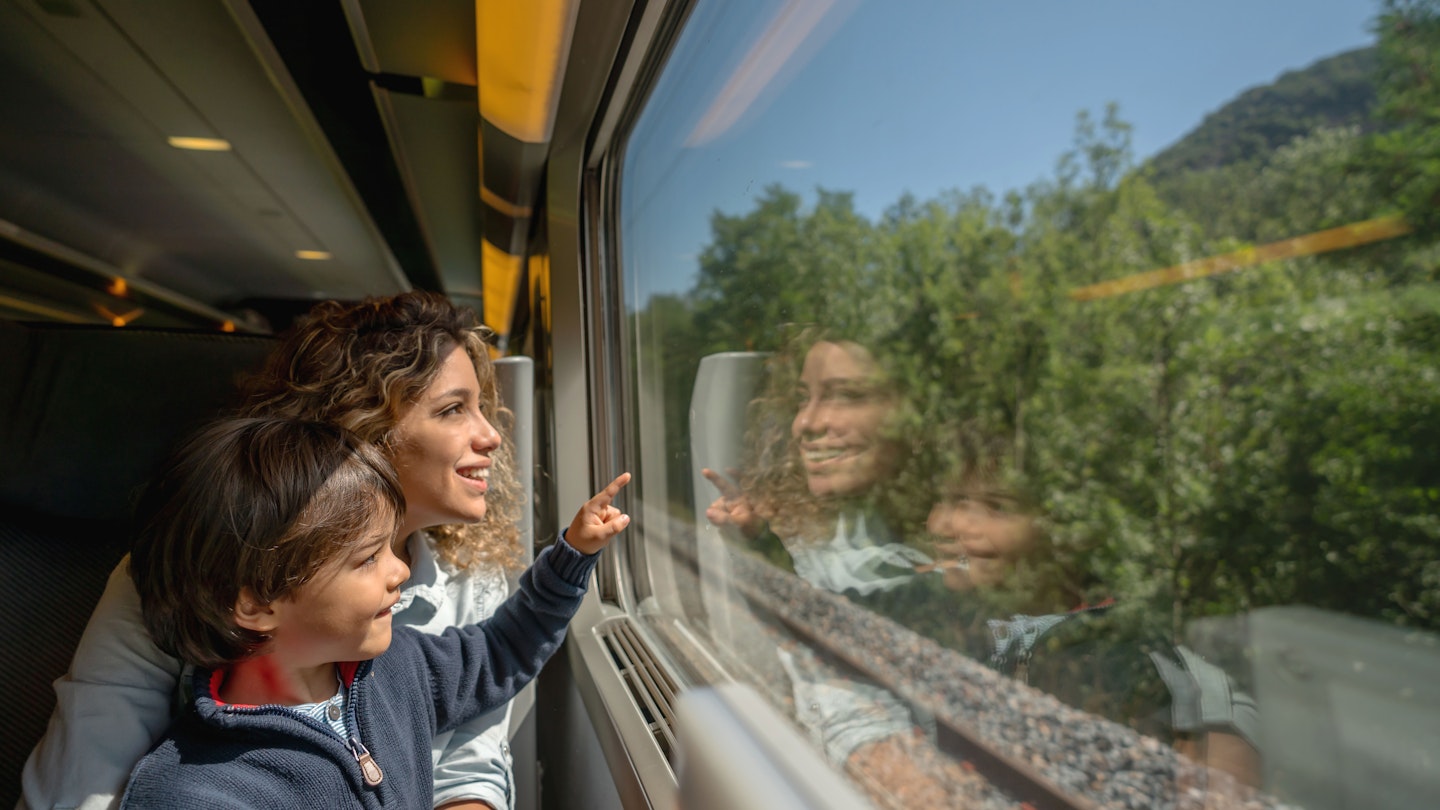 Portrait of a happy mother and son riding on the train and looking through the window while pointing away - transport concepts