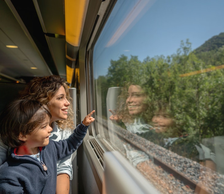 Portrait of a happy mother and son riding on the train and looking through the window while pointing away - transport concepts