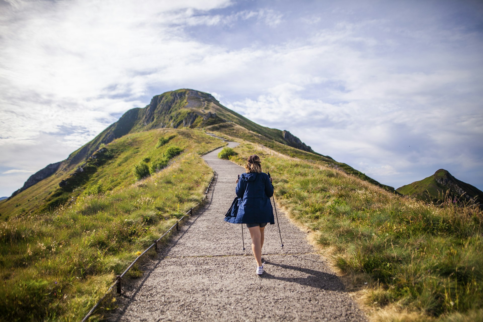A woman hikes up a path towards a mountain peak