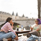 Friends talking while sitting near to Seine river in Paris, France.

