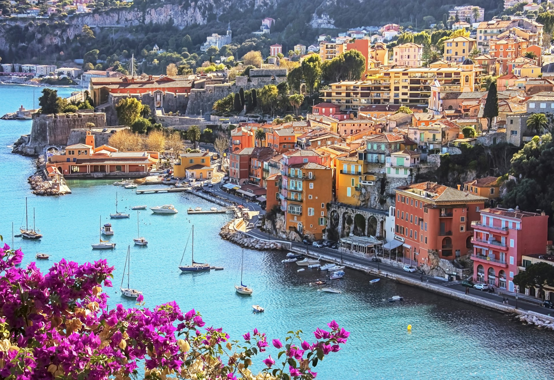 A view of Villefranche-sur-Mer village, with yachts and purple bougainvillea, in Côte d’Azur, France
