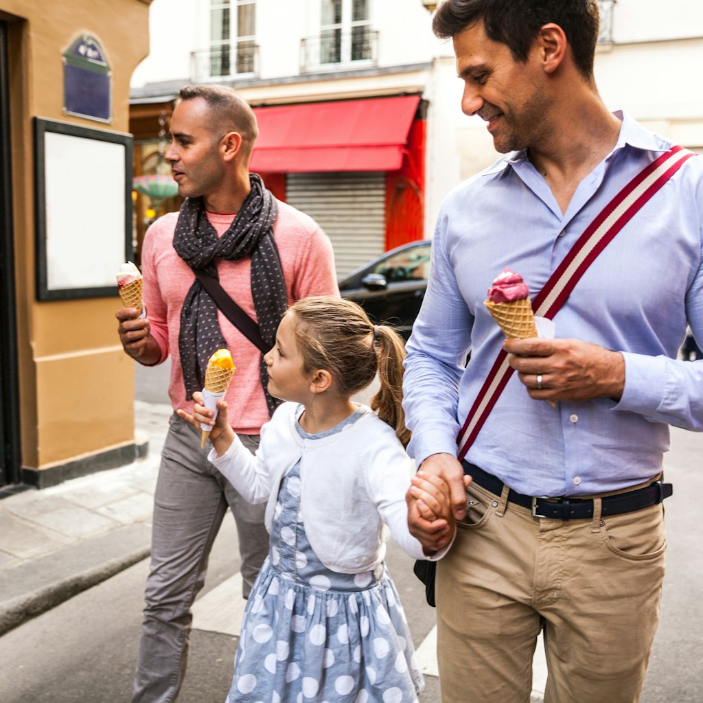 Gay male couple family spending a day outdoor in Paris downtown with young daughter, France.