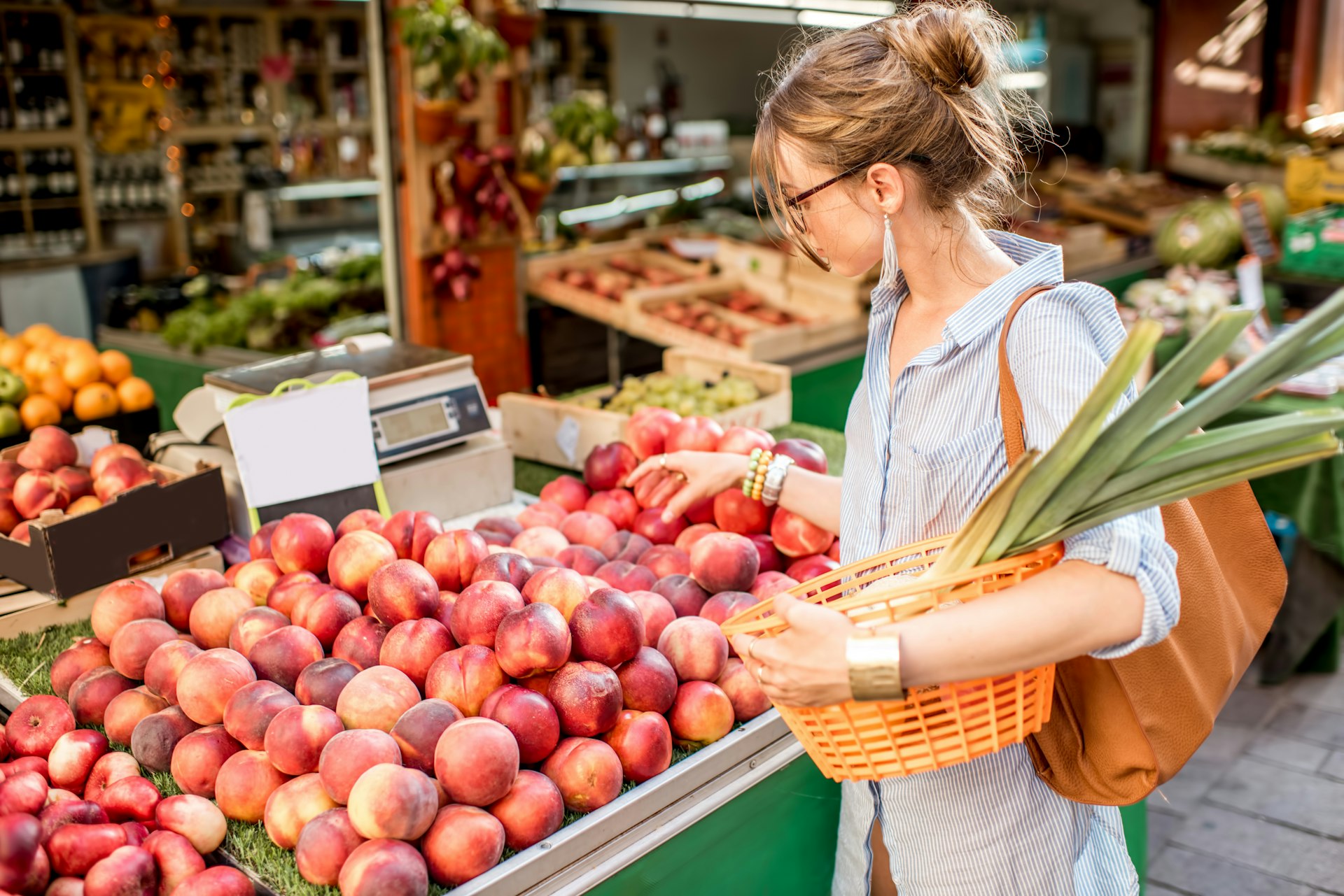 Young woman choosing a fresh peach standing with basket at an outdoor food market in France