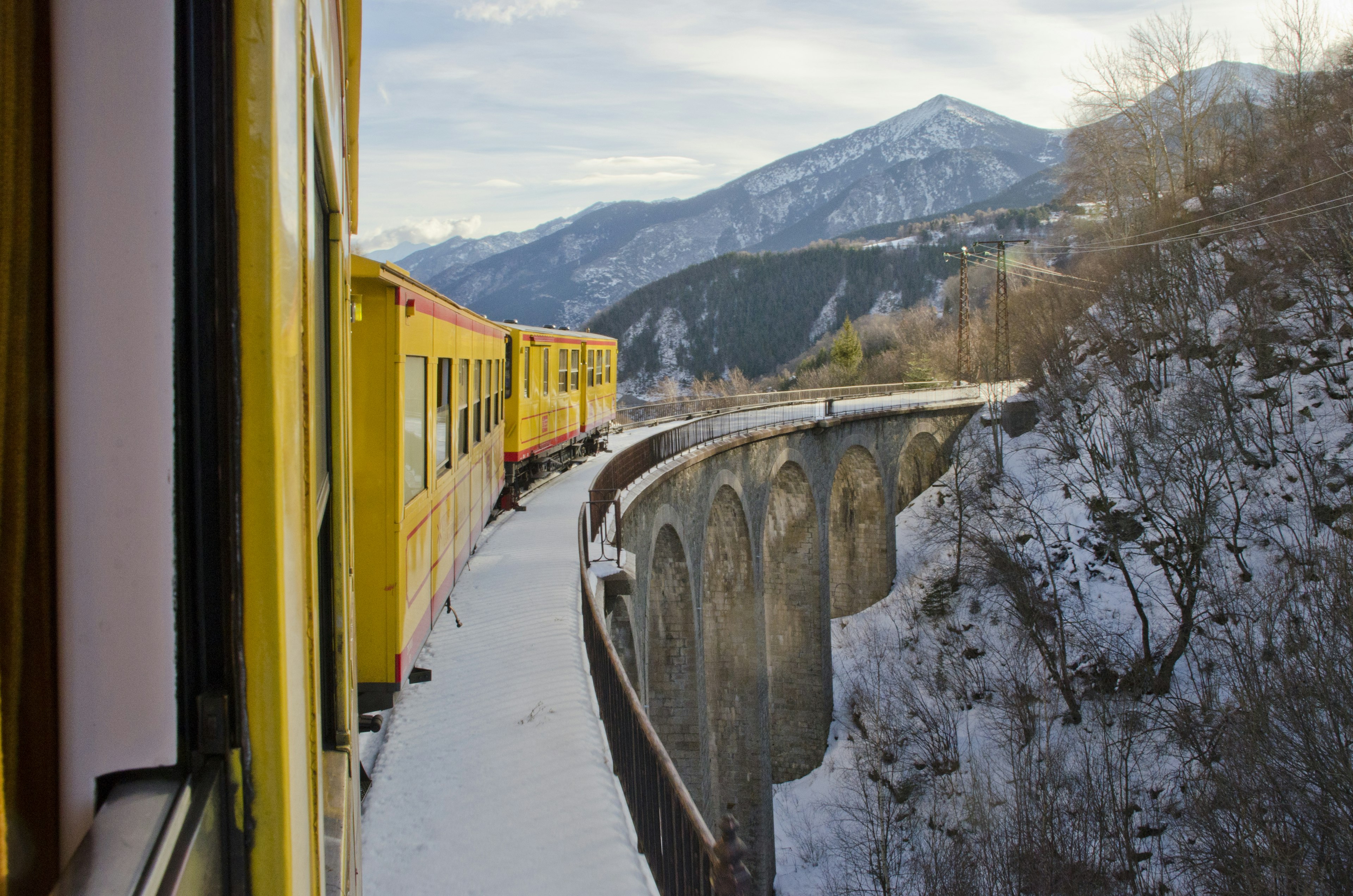 Train jaune passing on a bridge in a snowy landscape at the French Pyrenees