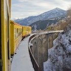 Train jaune passing on a bridge in a snowy landscape at the French Pyrenees
