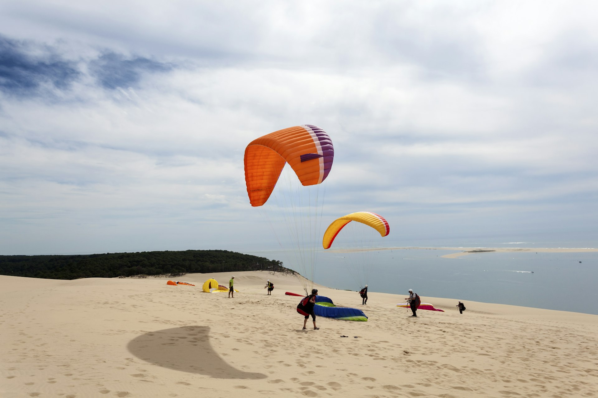 A paraglider prepares to head out from the top a sand dune